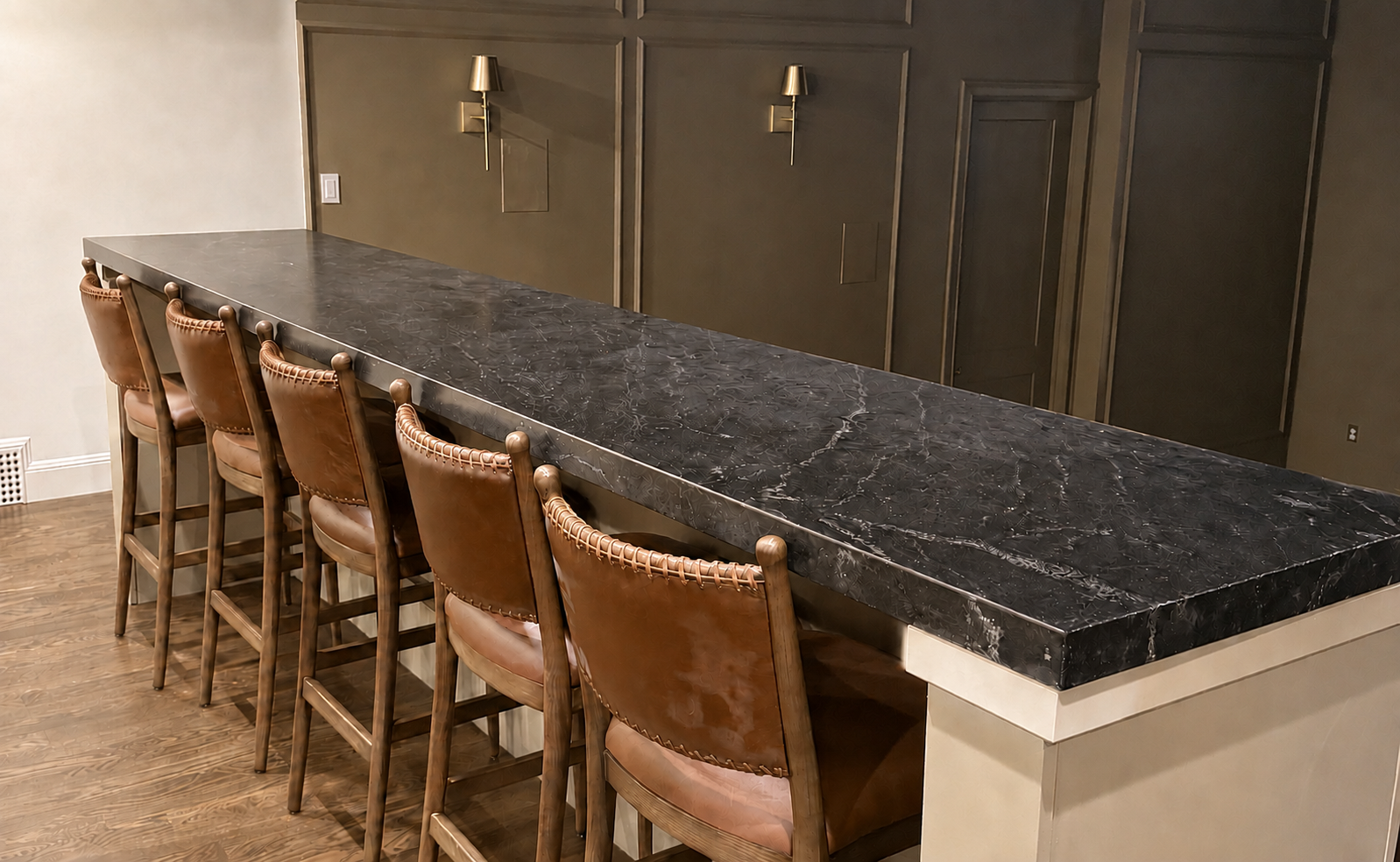 Long stone-topped dining counter with several wooden bar stools in a modern kitchen area