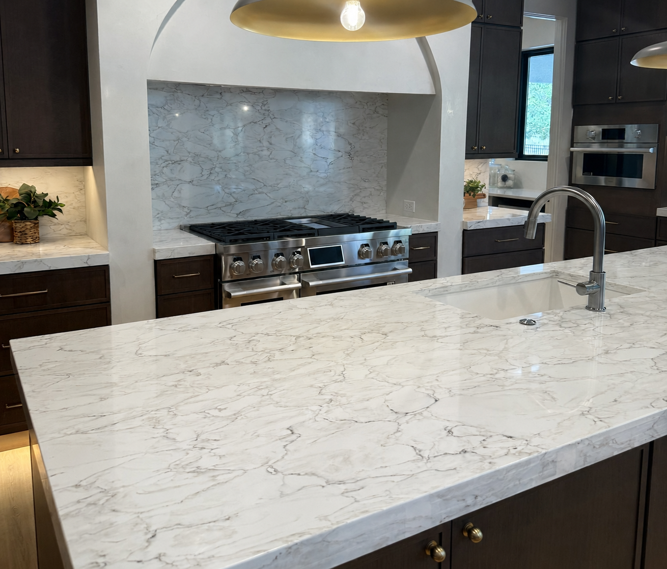 Modern kitchen with white marble island, stainless range, dark cabinets, and pendant light