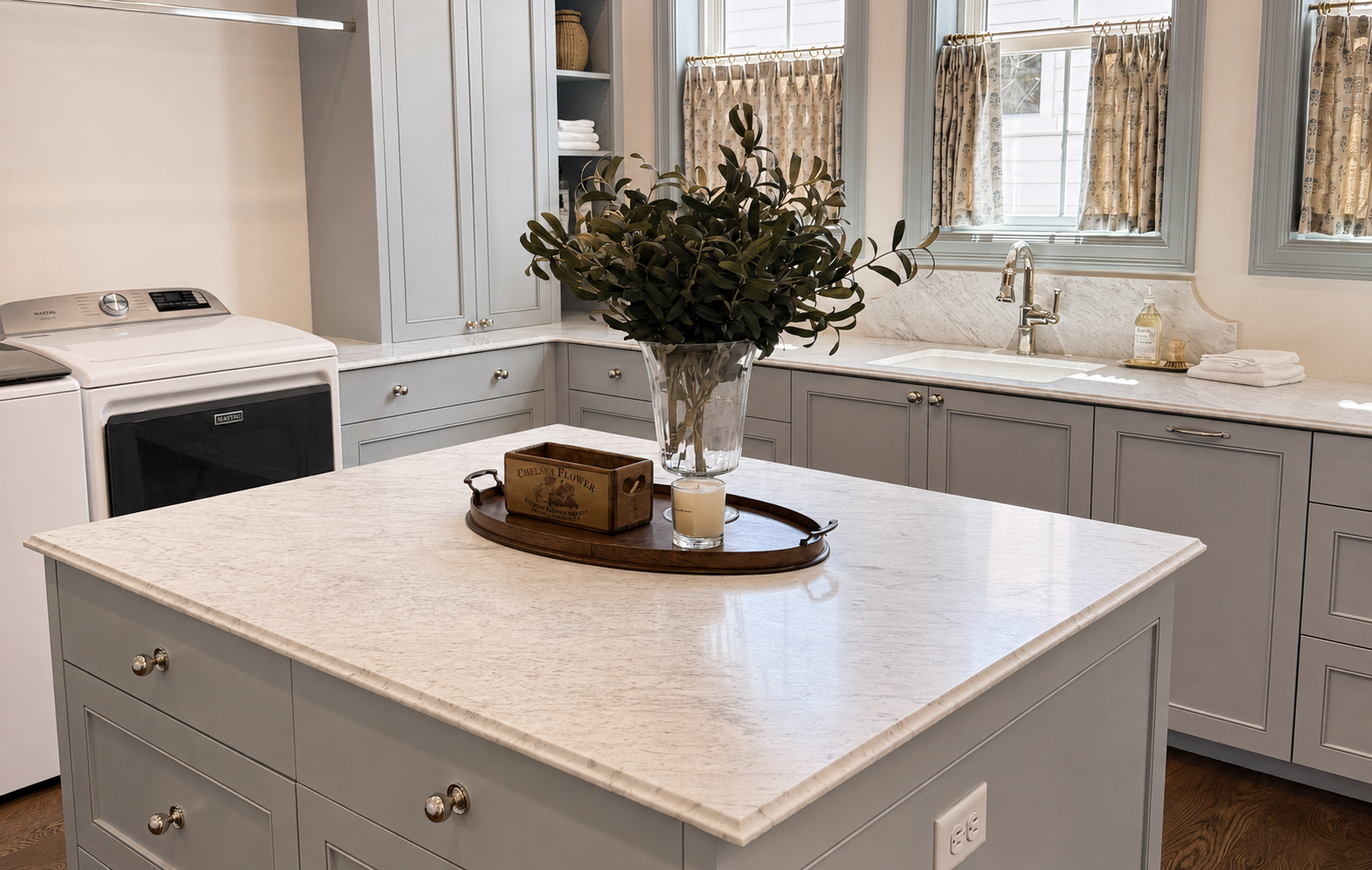 Bright kitchen with a large gray island, white cabinets, and a round tray centerpiece by the window.