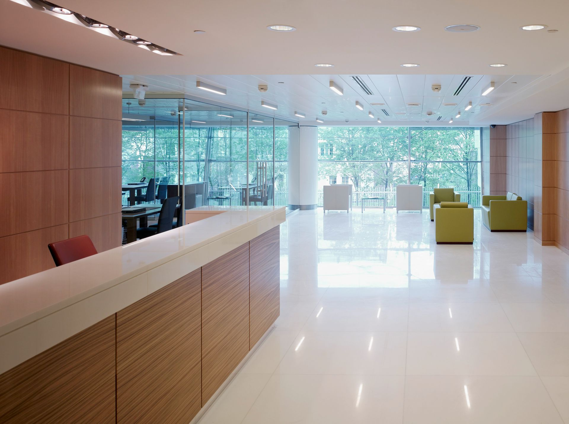 Modern empty office lobby with glossy white floor, wood reception desk, and large windows overlooking trees
