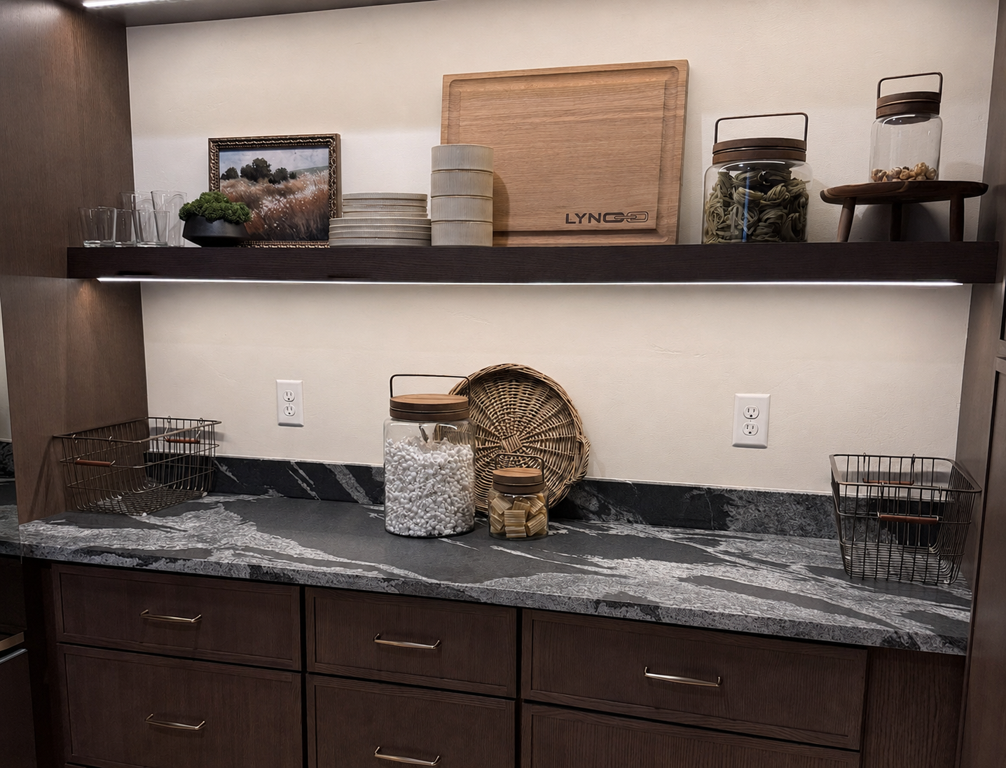 Decorative kitchen counter with shelves, baskets, jars, and a wooden crate against a light wall