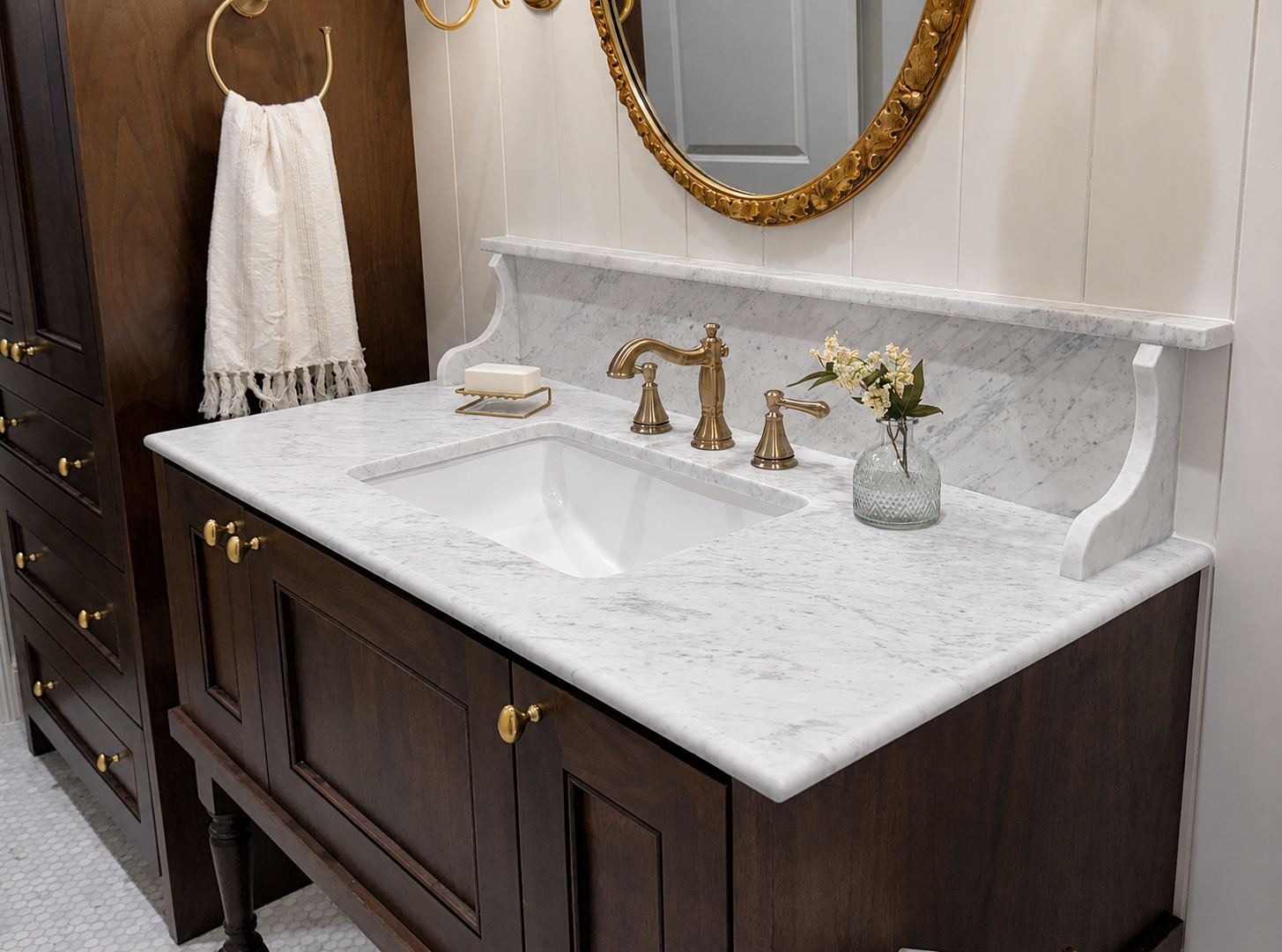 Elegant bathroom vanity with white marble countertop, gold fixtures, round mirror, and dark wood cabinets