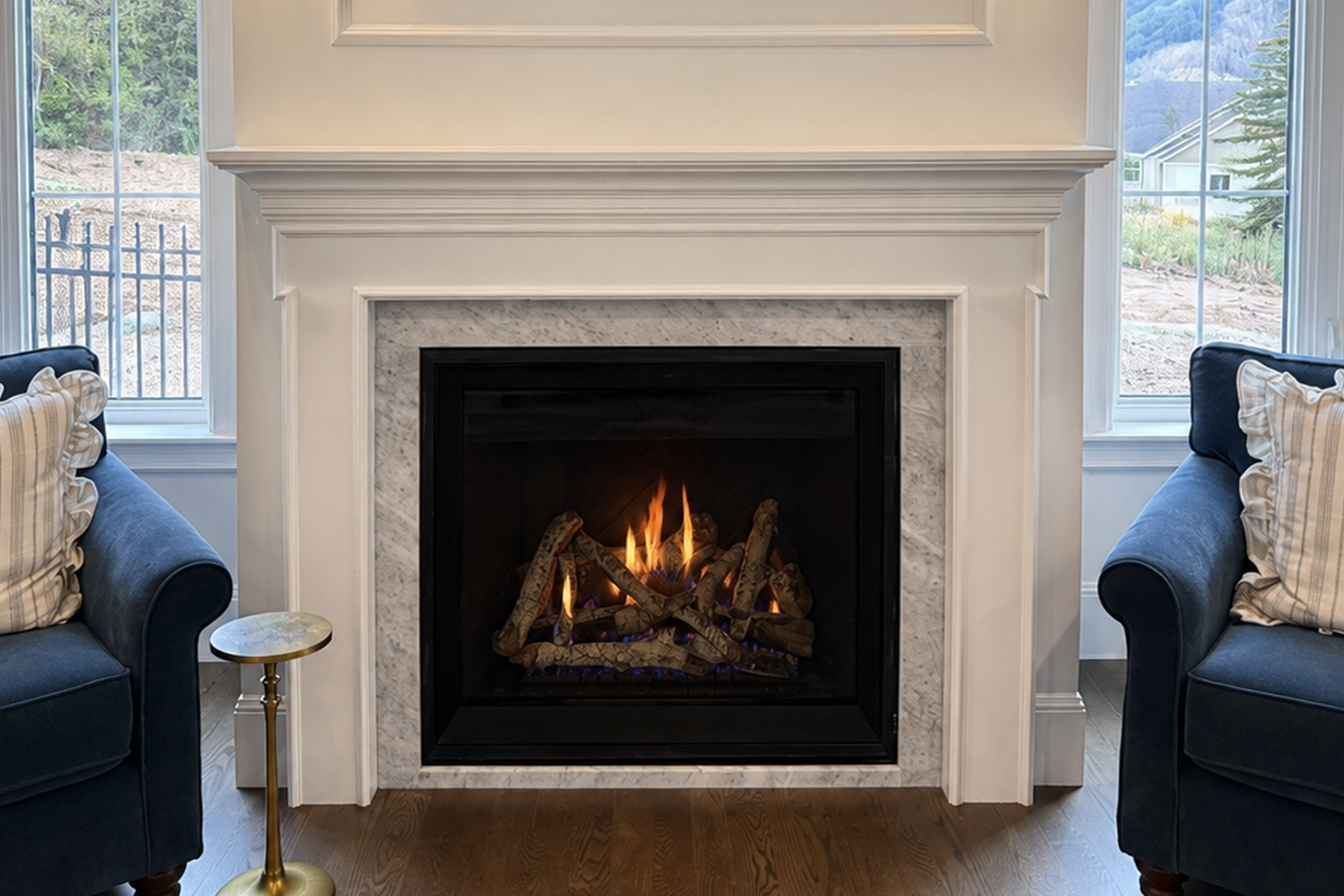 Modern living room fireplace with a lit fire, framed by white mantel and blue chairs beside windows