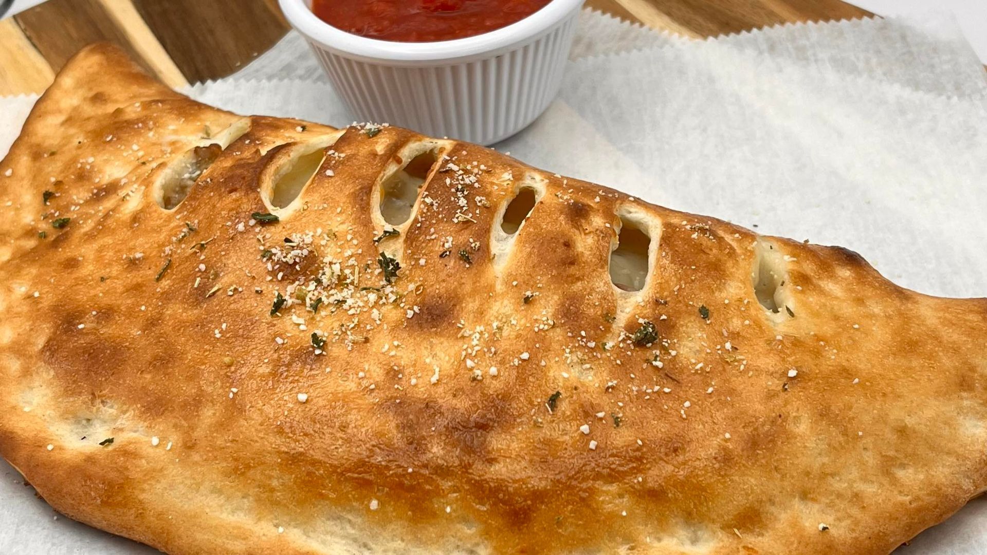 A close up of a stromboli on a plate next to a bowl of marinara.