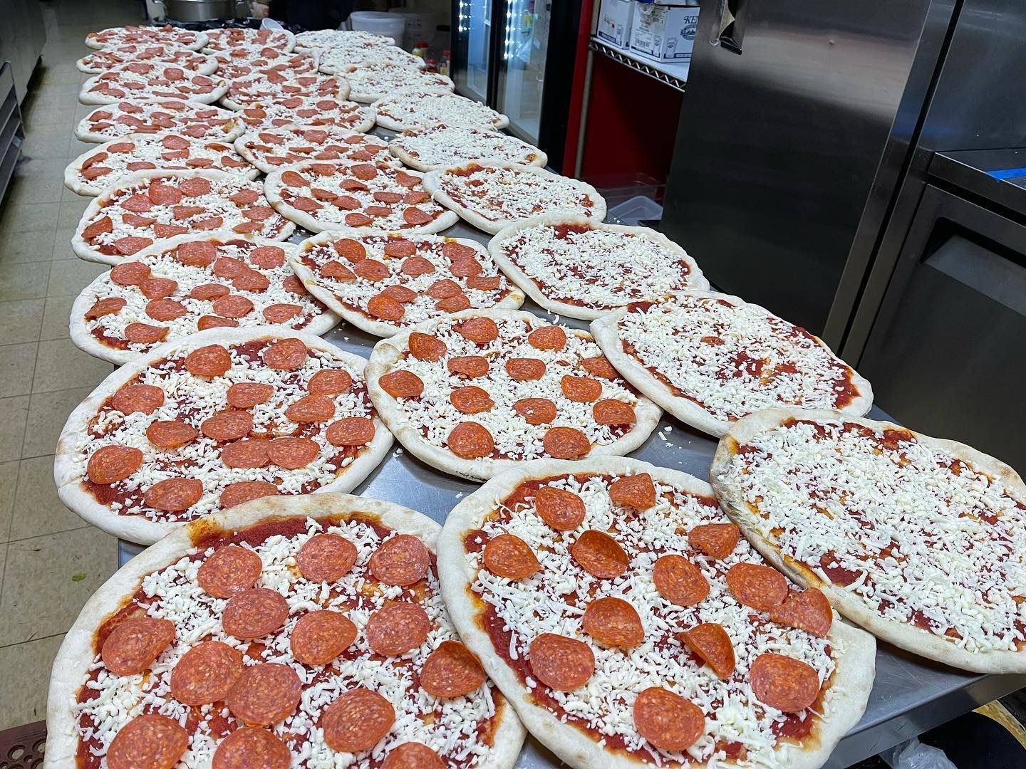A row of pepperoni pizzas sitting on top of a metal tray.