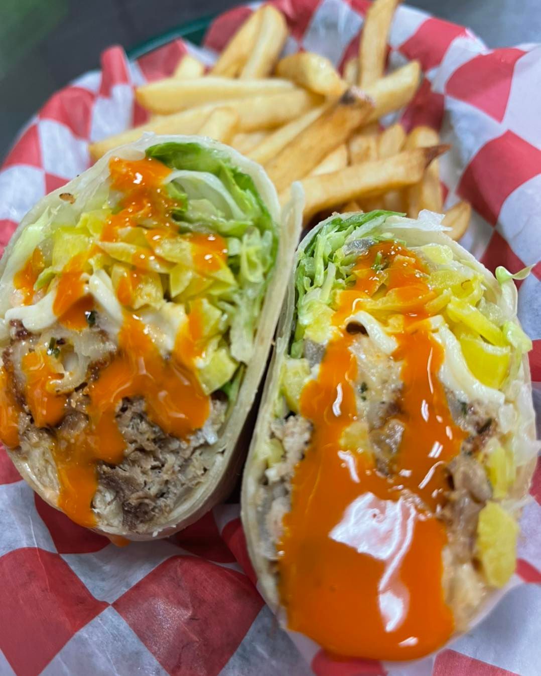 Two wraps with french fries on a checkered paper on a plate.