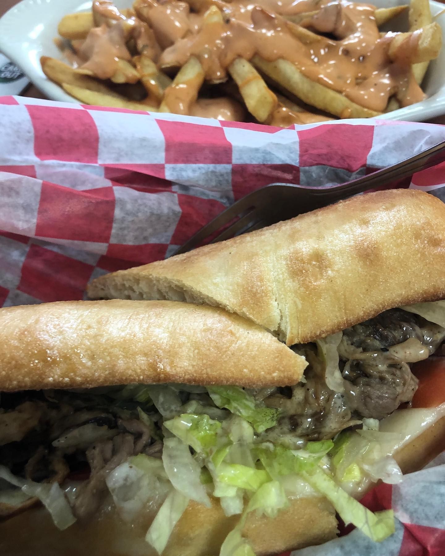 A sub sandwich is sitting on a table next to a plate of french fries.