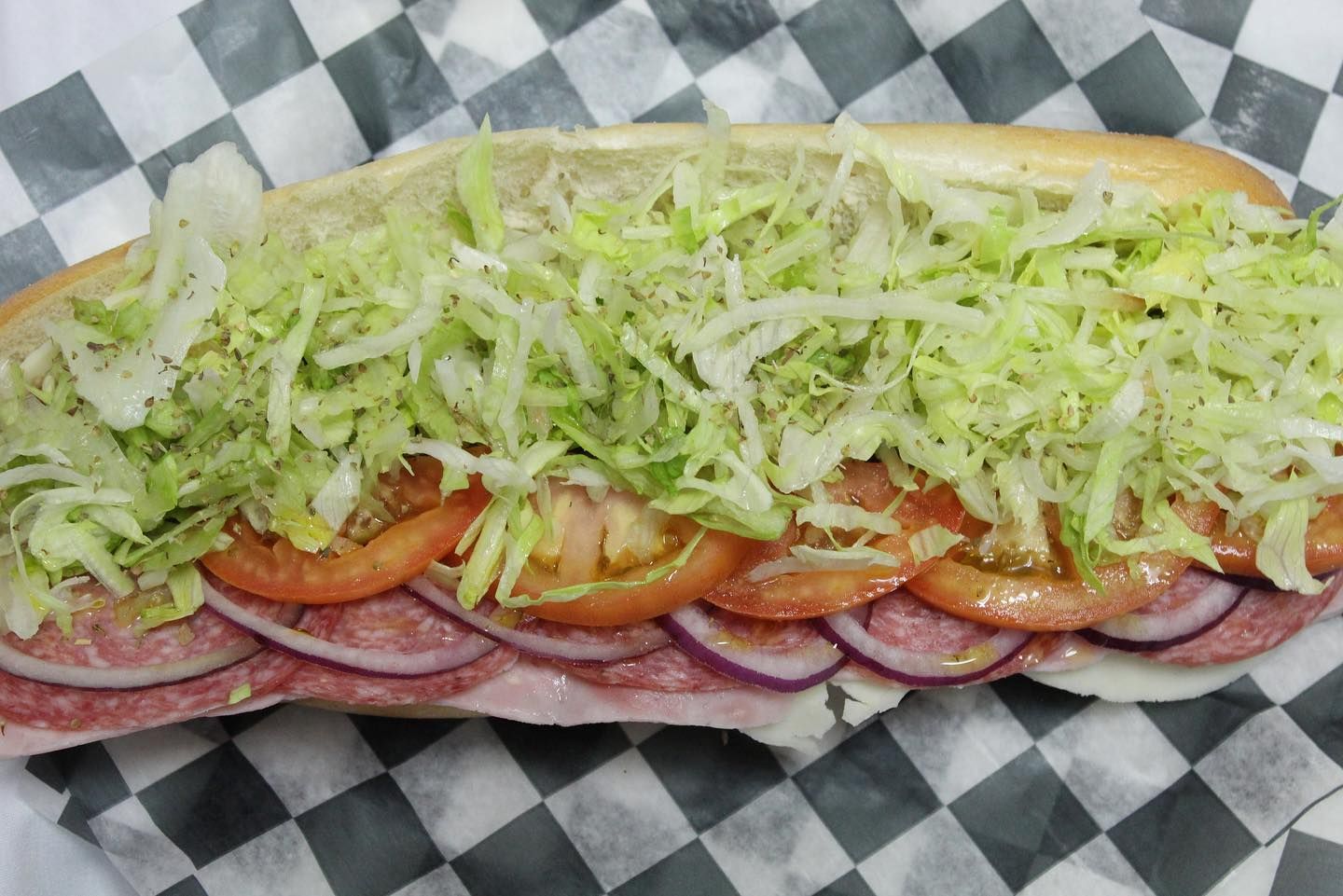 A sub sandwich with lettuce , tomatoes , onions and cheese is sitting on a checkered napkin.