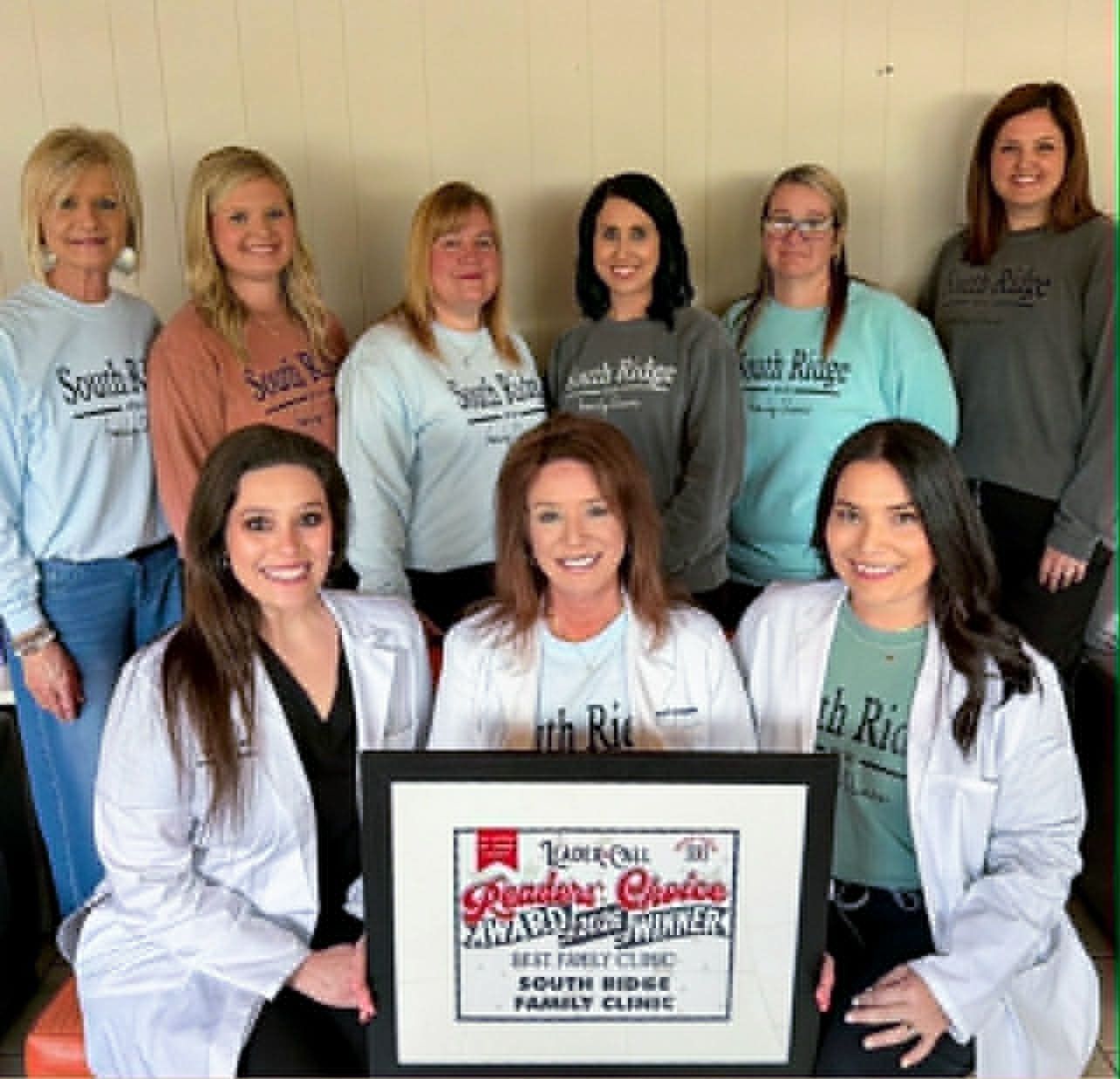 Team of clinic staff posing with a framed award plaque indoors.