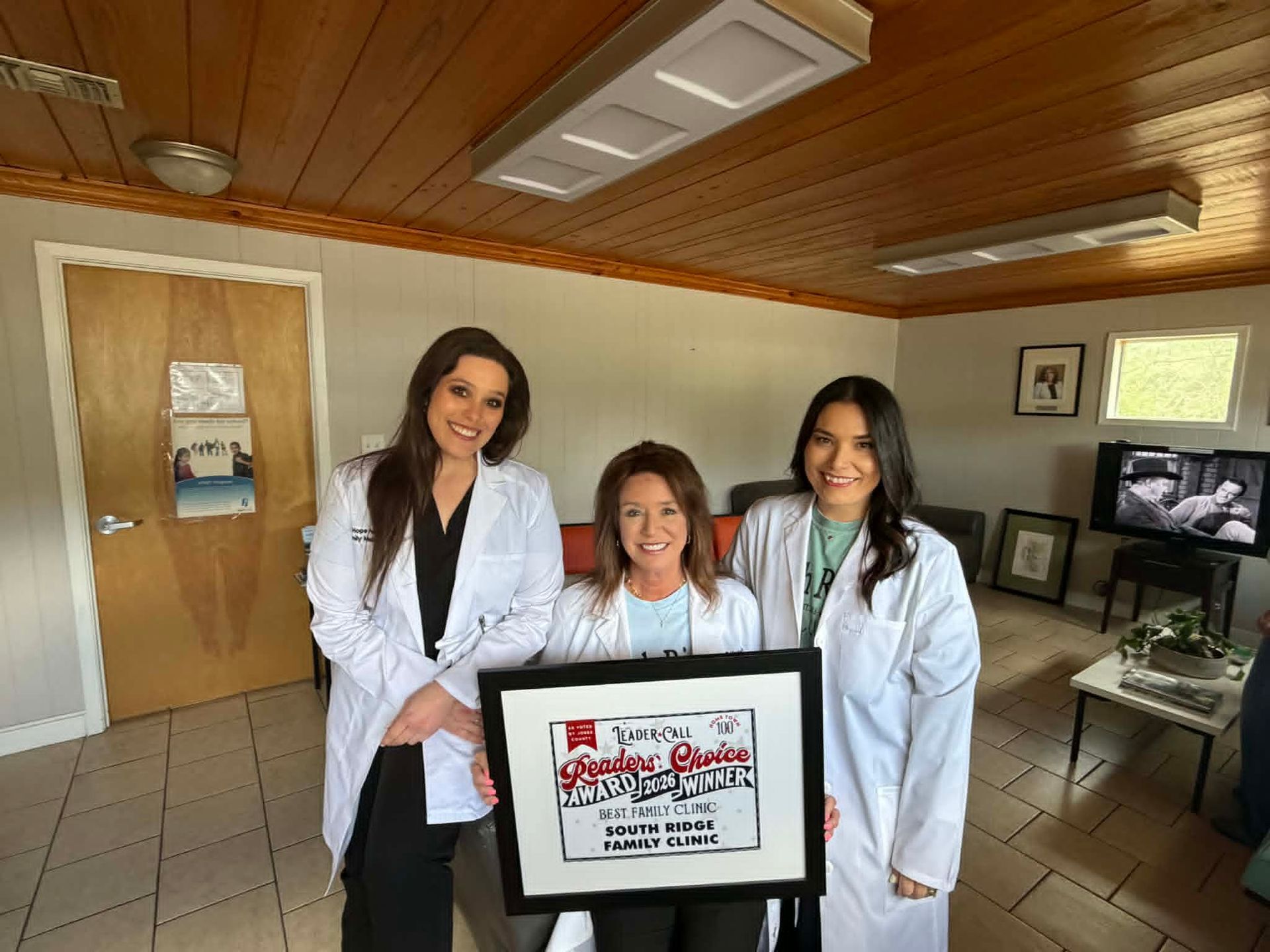 Three people in white coats hold a framed award in a wood-paneled room.