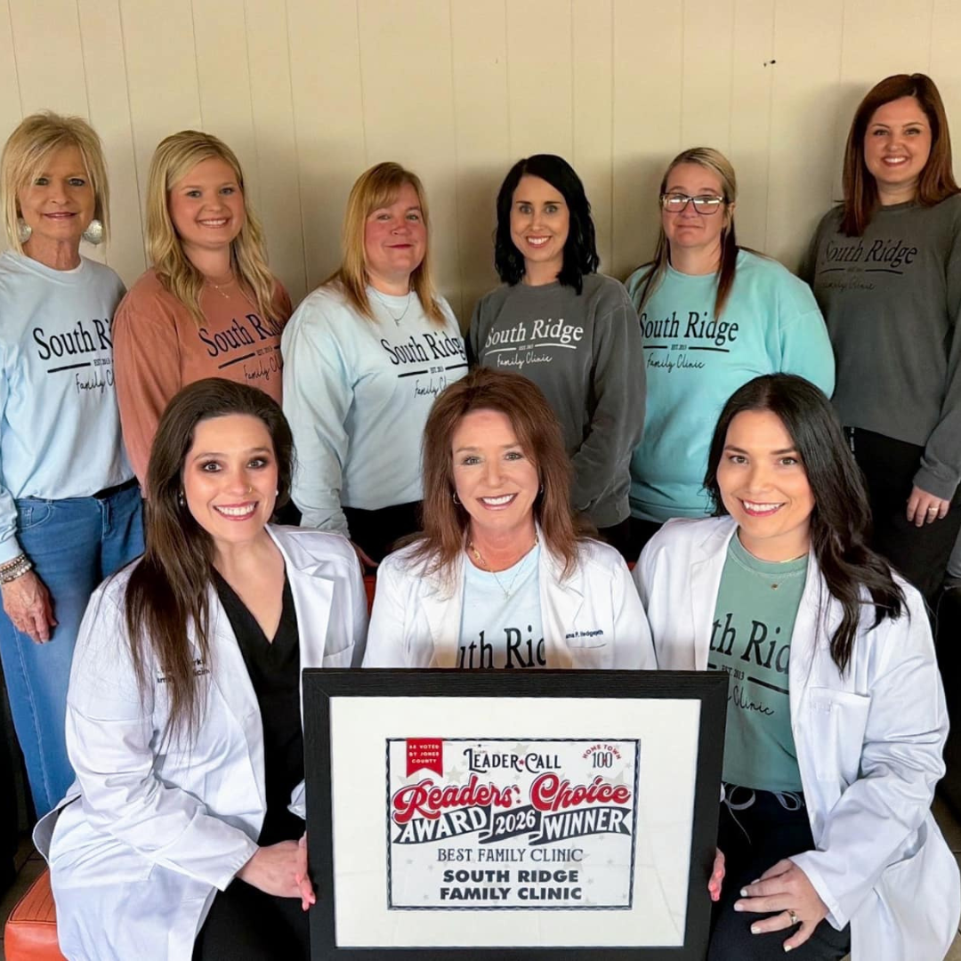 Group of smiling clinic staff posing indoors, with two women holding an award plaque in front.