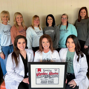 Nine women in clinic shirts pose indoors, holding a framed award plaque.