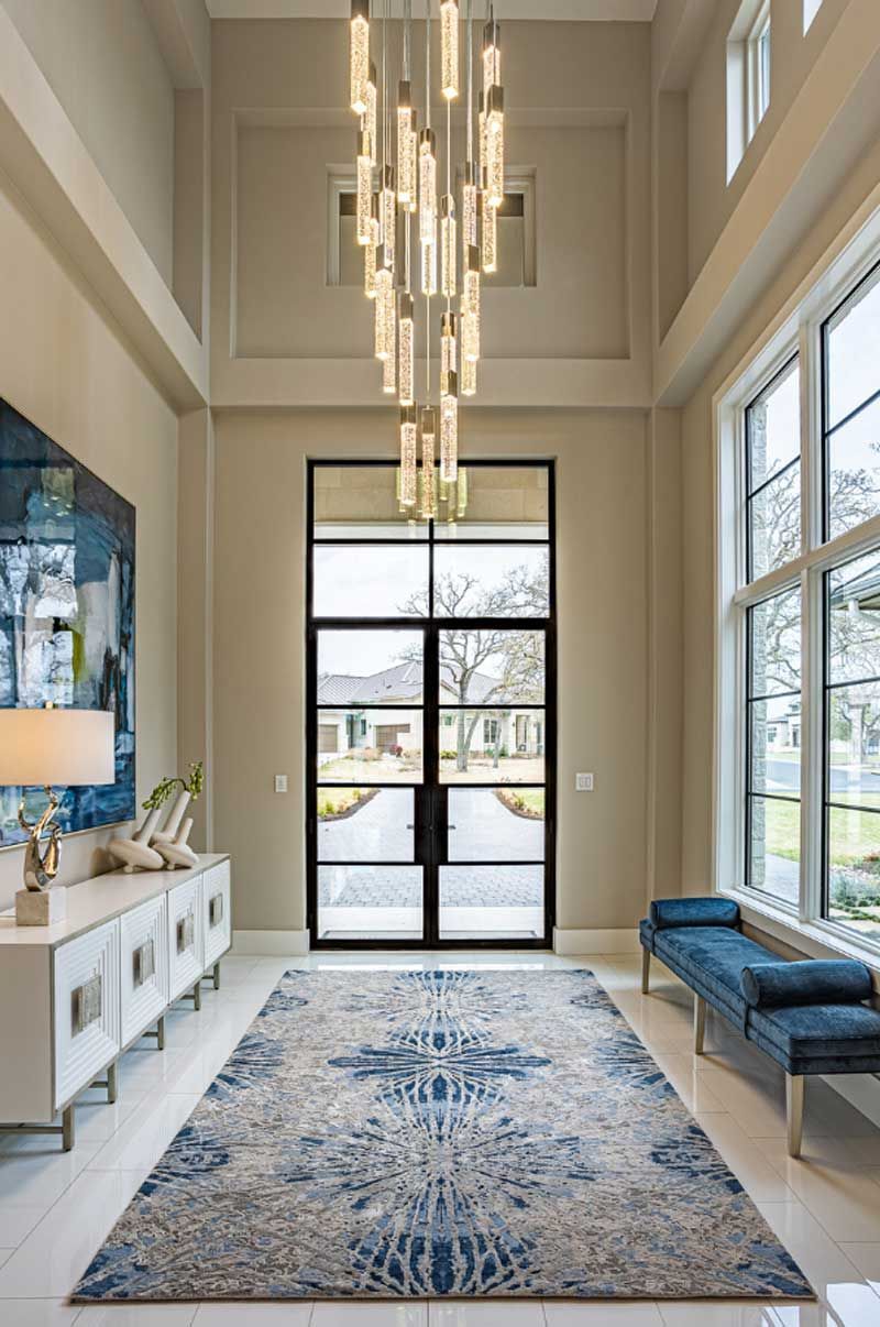 Bright modern hallway with tall windows, pendant lights, blue bench, patterned rug, and console table