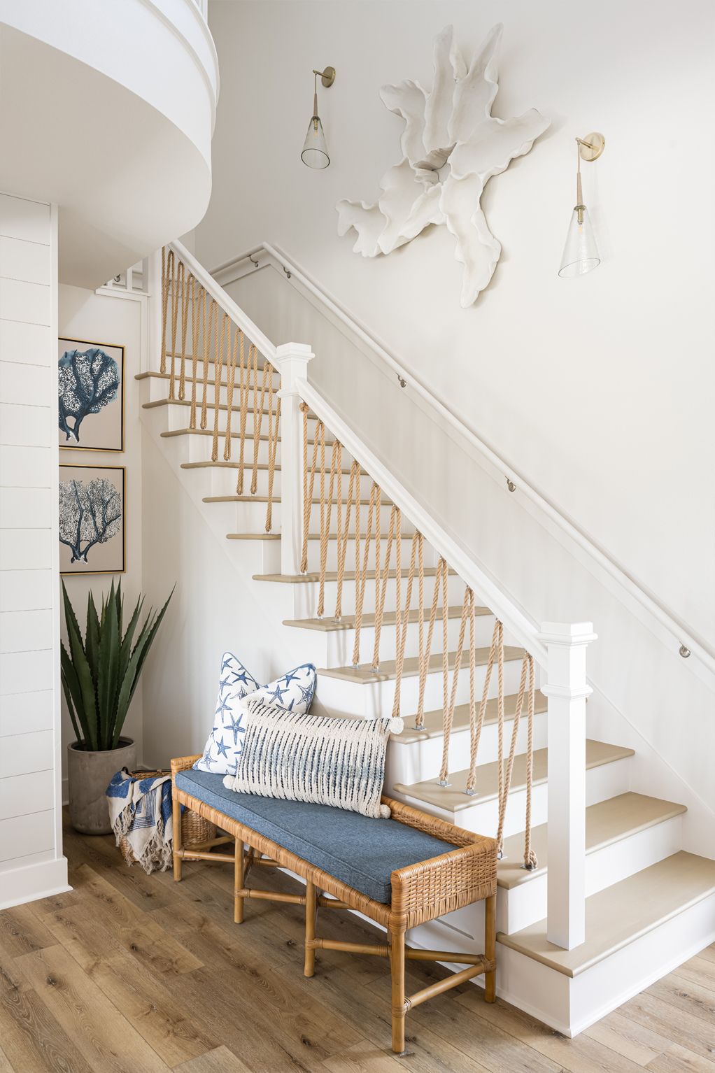 Bright white staircase with wicker bench, blue cushion, and wall-mounted deer decor in a cozy entryway