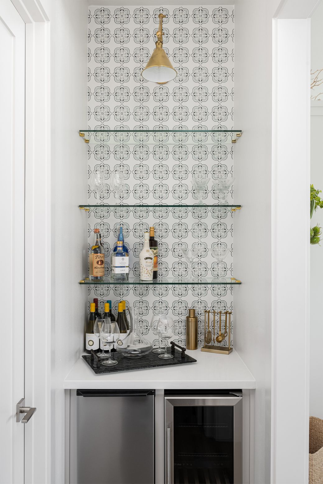 Built-in bar nook with patterned tile wall, glass shelves, bottles, and a mini fridge below