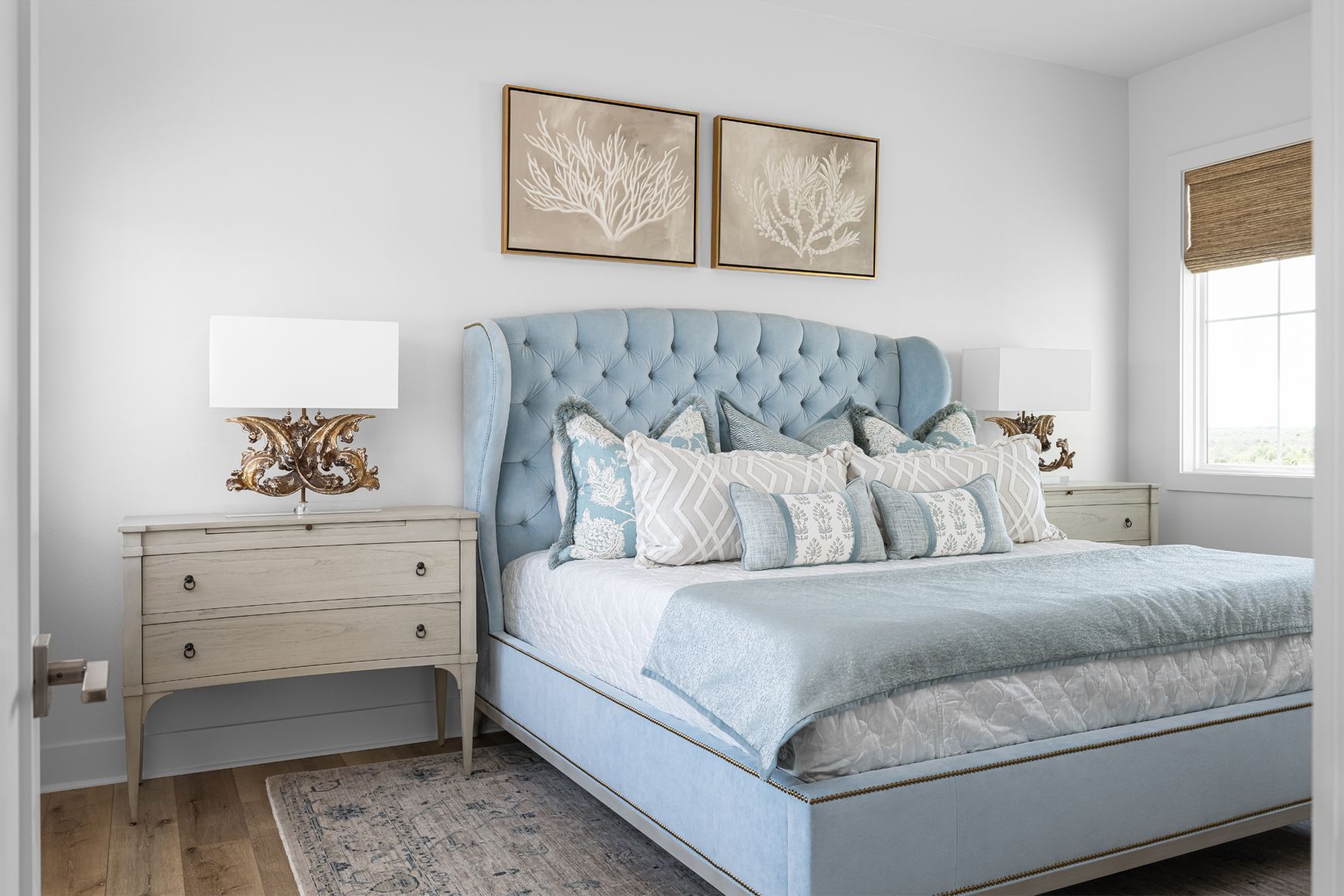 Bright bedroom with light blue tufted bed, white nightstand, and neutral decor