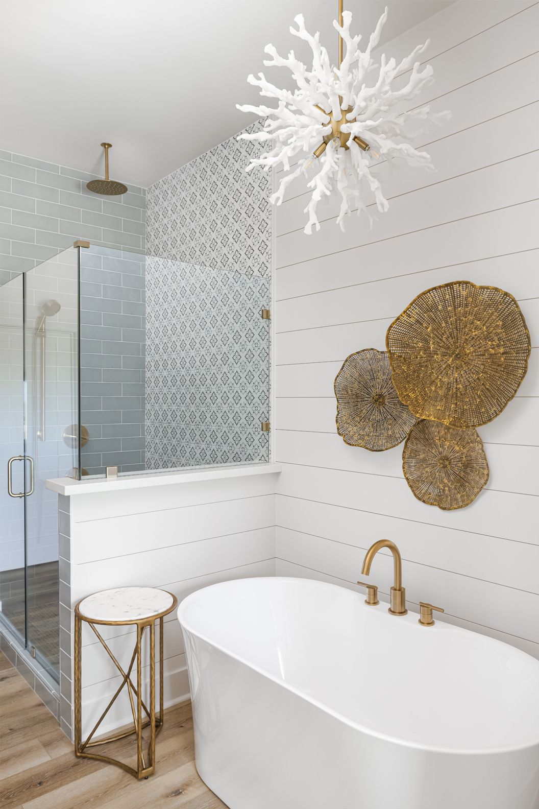 Modern bathroom with white shiplap walls, freestanding tub, glass shower, gold accents, and starburst chandelier