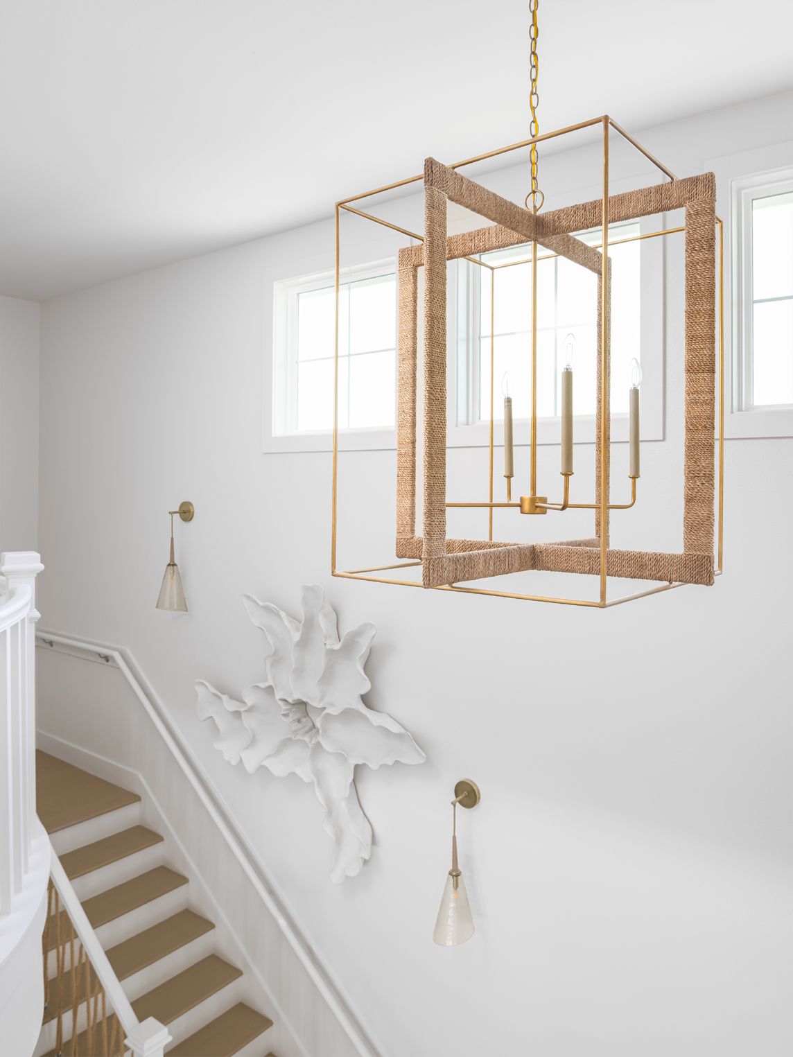 Gold geometric chandelier above a white staircase with decorative wall molding and windows