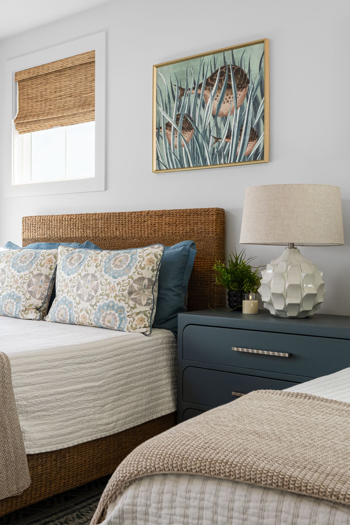Cozy bedroom with woven headboard, blue nightstand, patterned pillows, lamp, and framed artwork
