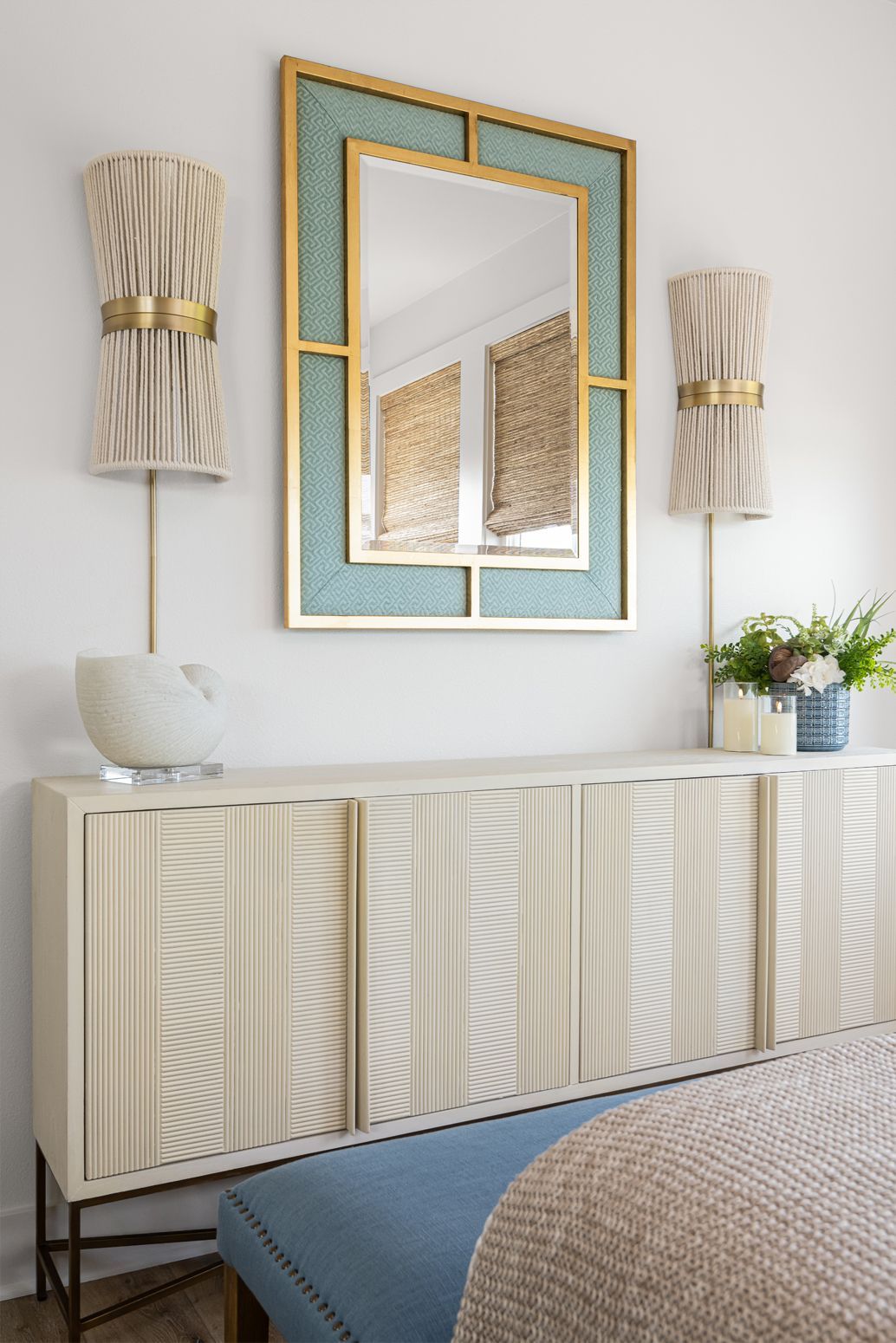 Stylish bedroom dresser with gold-framed mirror, wall sconces, lamp, and blue upholstered bench