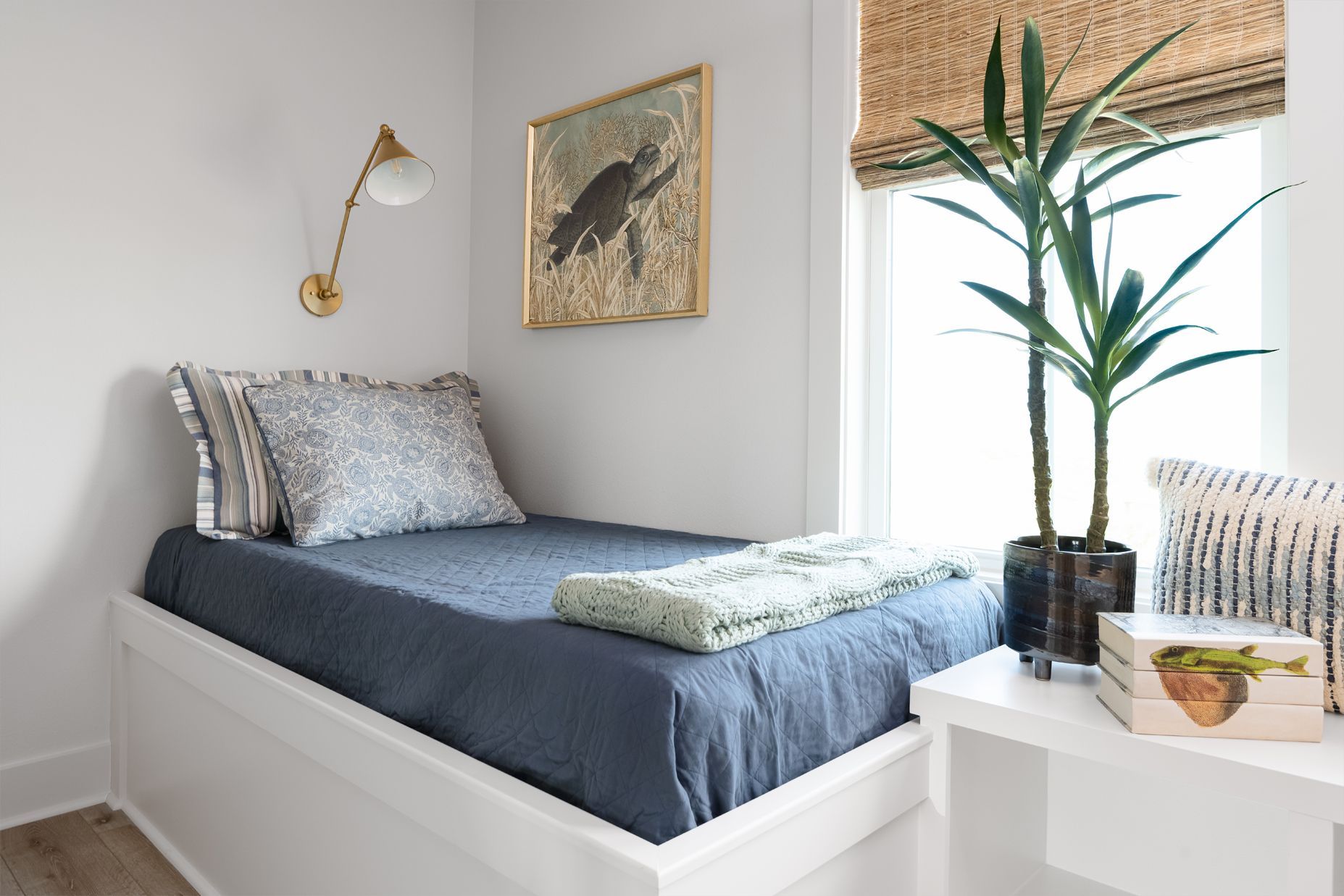 Bright bedroom with white bed, blue bedding, and a potted plant by the window