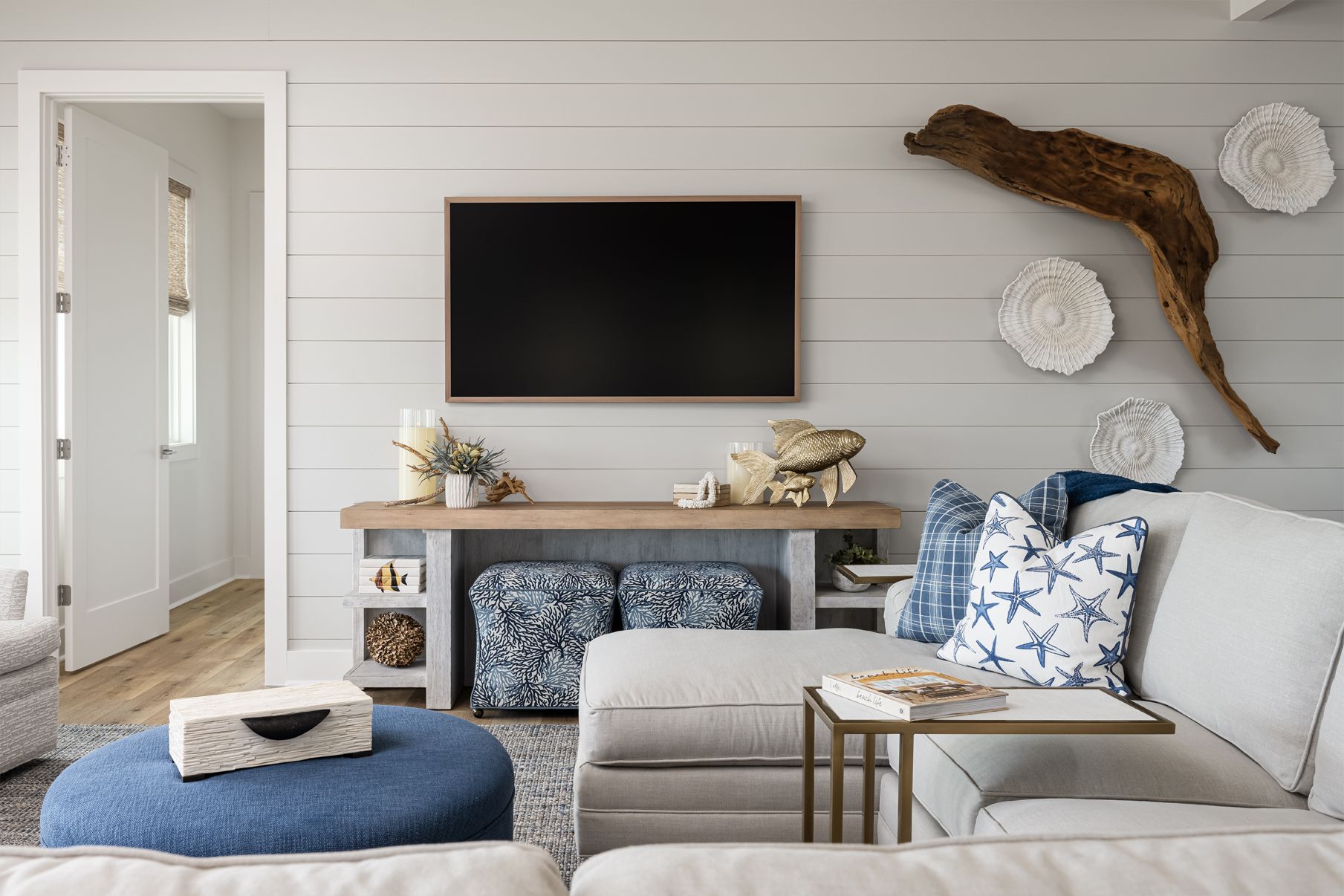 Bright living room with white shiplap walls, blue-and-white decor, wall-mounted TV, and gray sofa