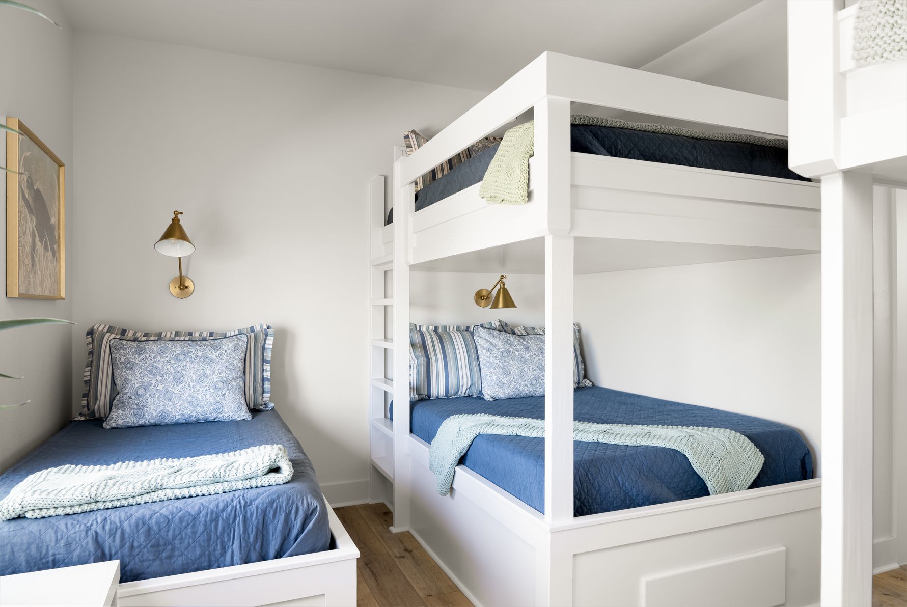 Bright white bedroom with blue bedding, two twin beds, and a white bunk bed in a simple, tidy space