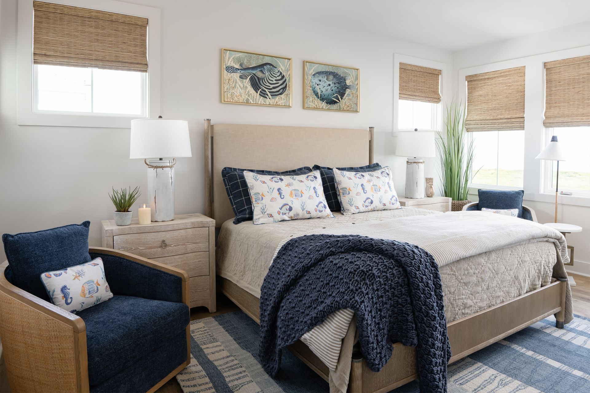 Bright bedroom with a navy bed, blue armchair, nightstand, and window blinds, styled in neutral tones