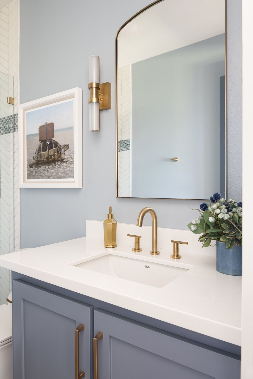Modern bathroom vanity with blue cabinets, gold fixtures, white countertop, and a large mirror