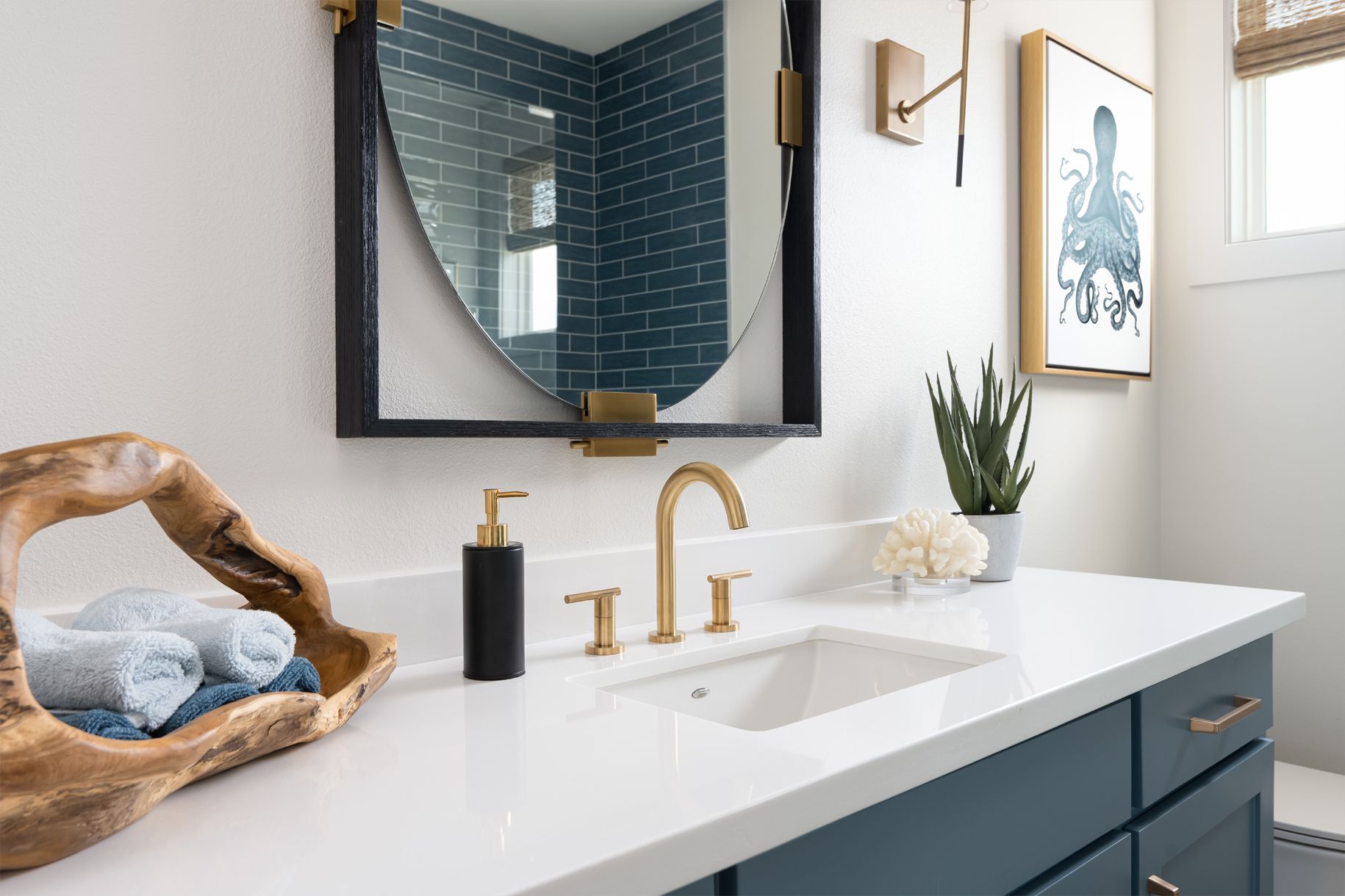 Modern bathroom vanity with white countertop, gold faucet, teal cabinets, mirror, and decorative accents