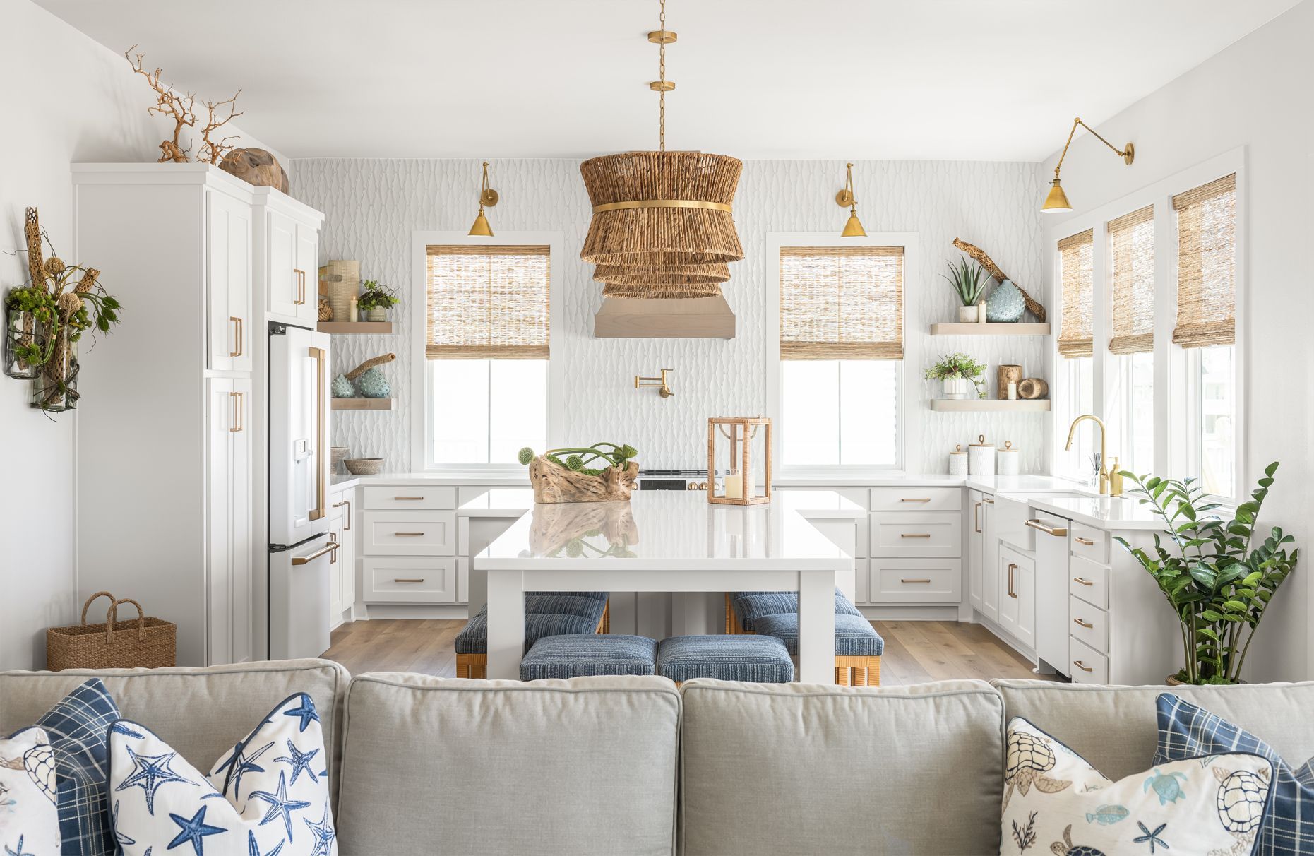 Bright white kitchen with an island, wicker pendant light, and beige sofa in the foreground.