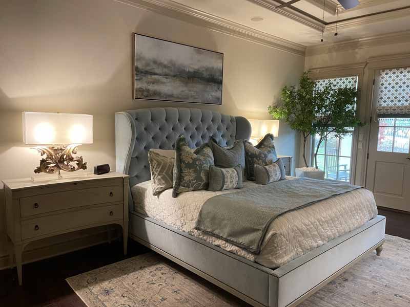 Elegant bedroom with a tufted blue bed, matching pillows, bedside lamps, and soft neutral decor