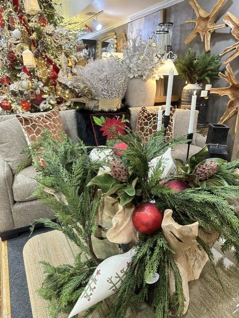 Festive floral arrangement with greenery, red ornaments, and ribbon in a decorated holiday room