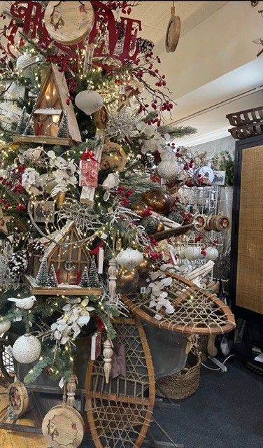 Decorated Christmas tree with ornaments, ribbons, and lights beside a wicker sleigh in a cozy indoor display