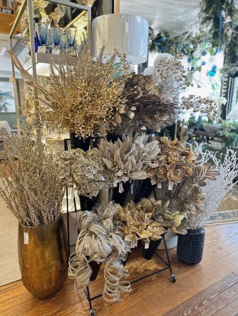 Dried floral arrangements in gold and black vases on a wooden table in a shop display