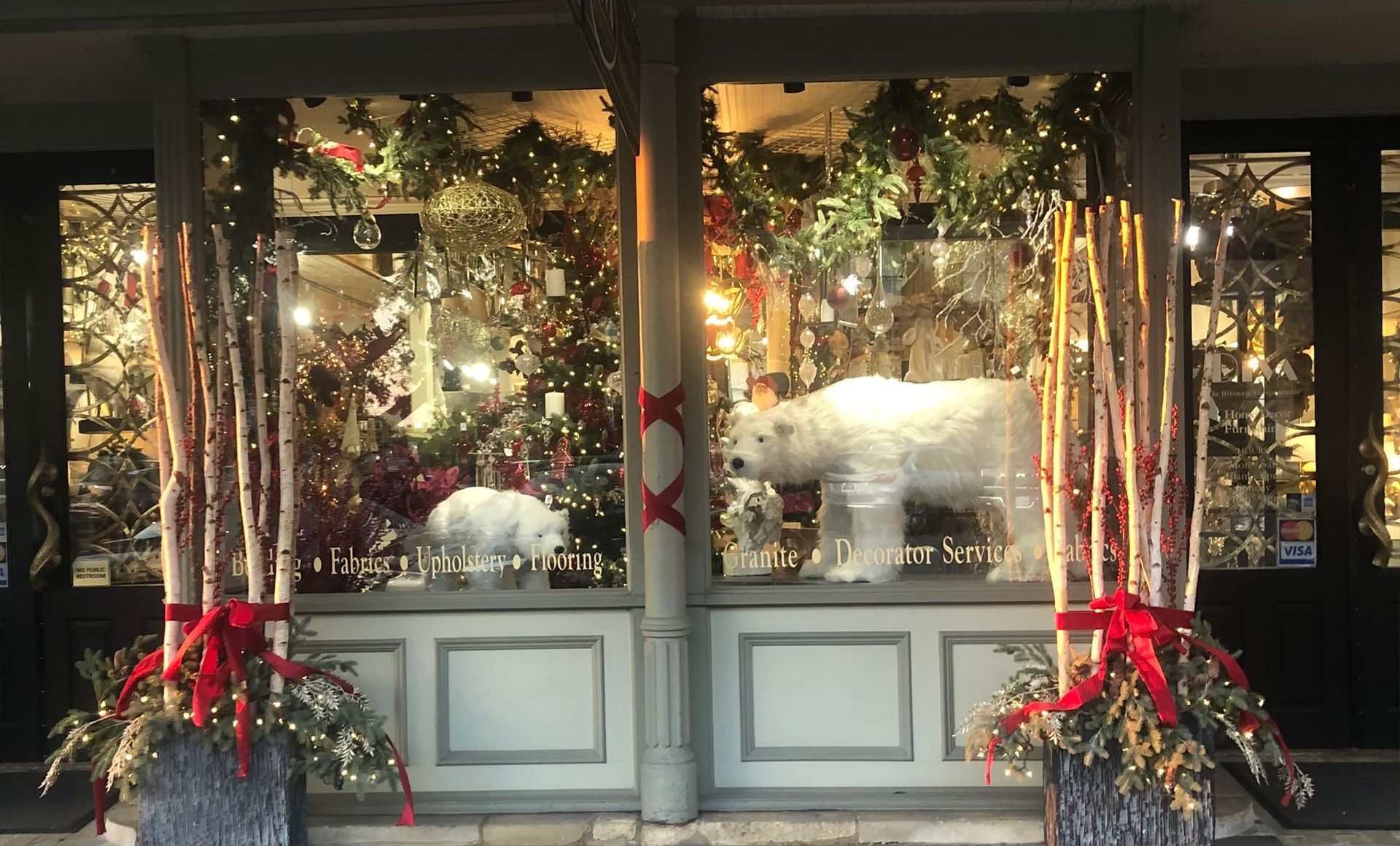 Festive storefront windows with Christmas wreaths, red bows, and holiday decorations illuminated at dusk