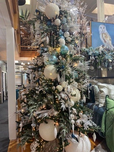 Tall decorated Christmas tree with white, gold, and blue ornaments in a bright indoor lobby