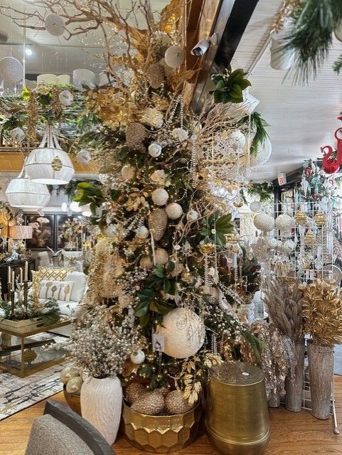 Festive gold-and-white holiday display with ornaments, branches, vases, and mirrored decor in a shop