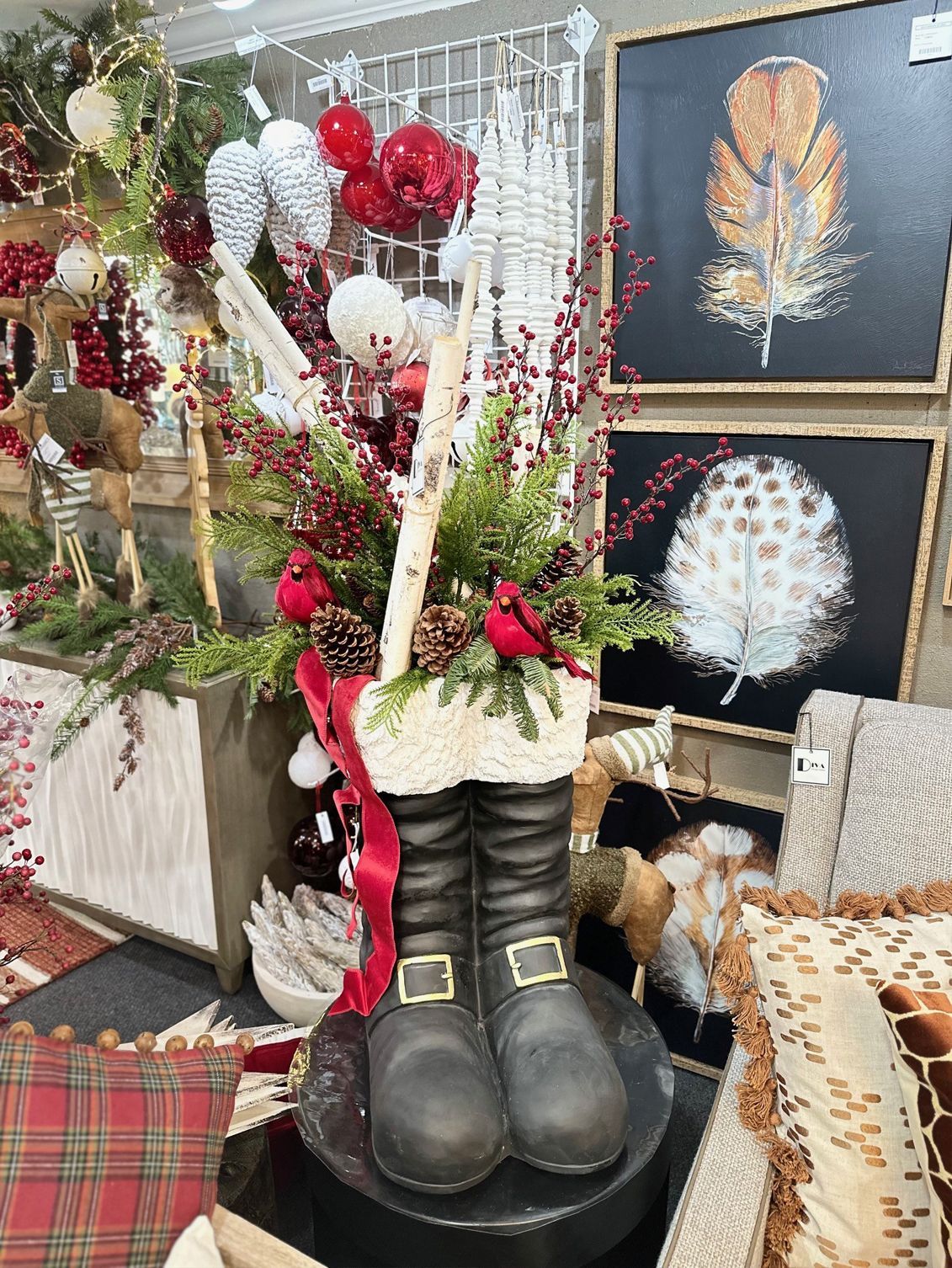 Black boots in a holiday display with red and white ornaments, garlands, and framed winter artwork