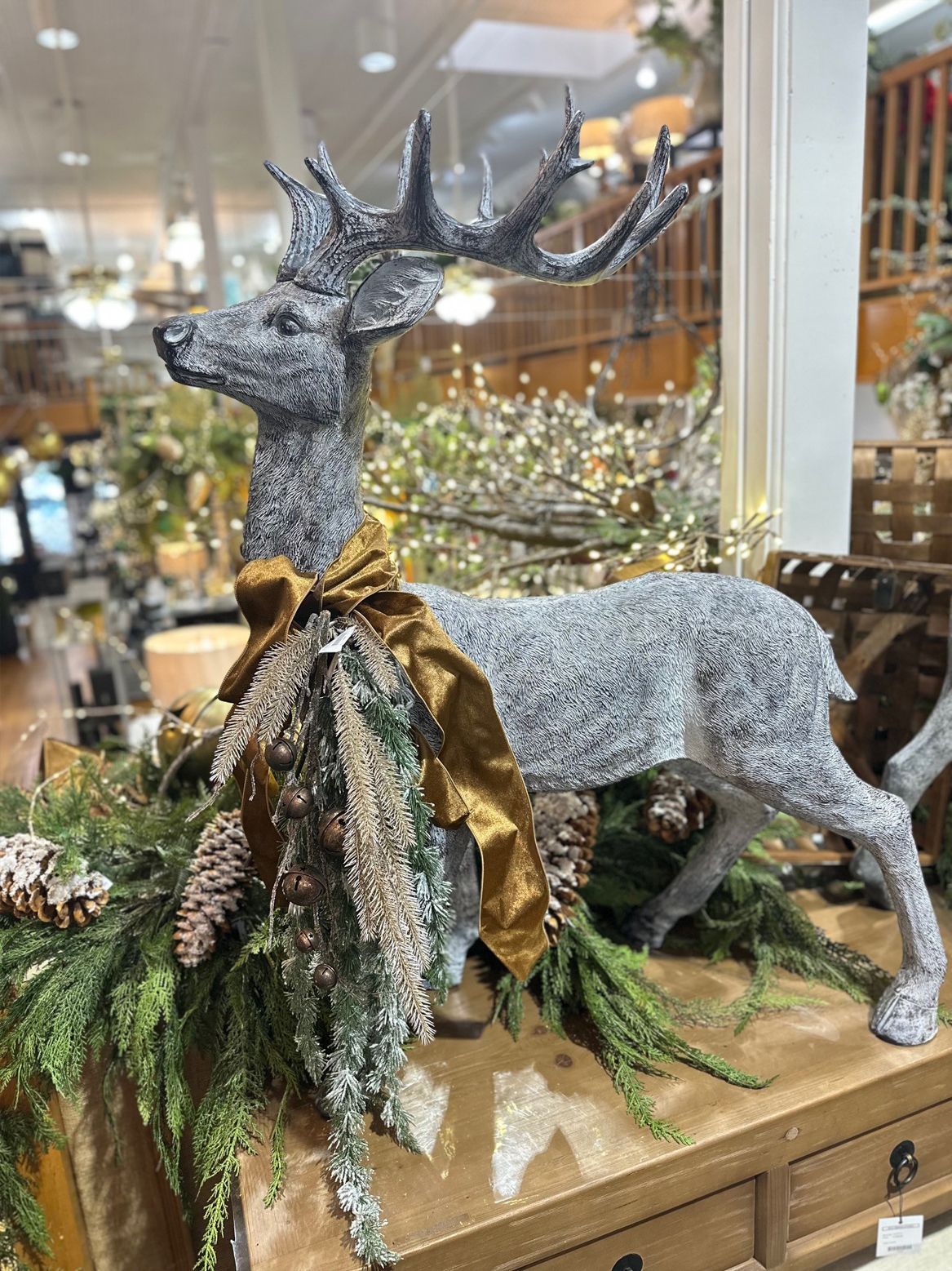 Sparkly silver reindeer holiday display with gold ribbon, greenery, and lights in a store window