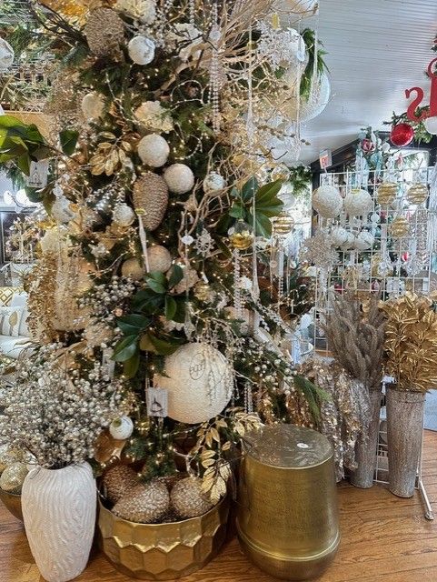 Decorated holiday tree display with white, gold, and silver ornaments, garlands, and vases in a store.
