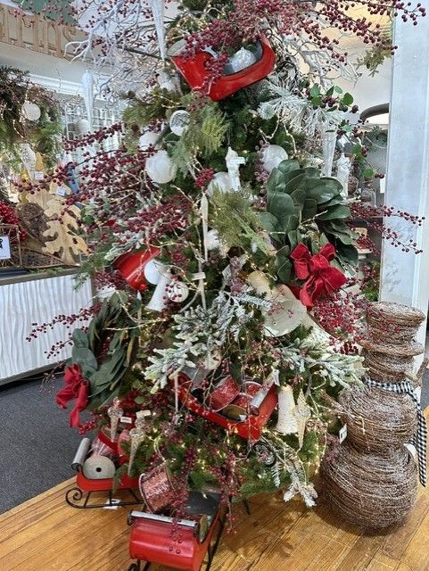 Decorated Christmas tree with red bows, white ornaments, and greenery in a shop or lobby