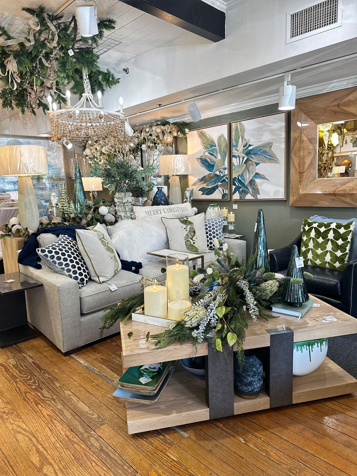 Decorative living room display with a sofa, coffee table, candles, greenery, and framed wall art