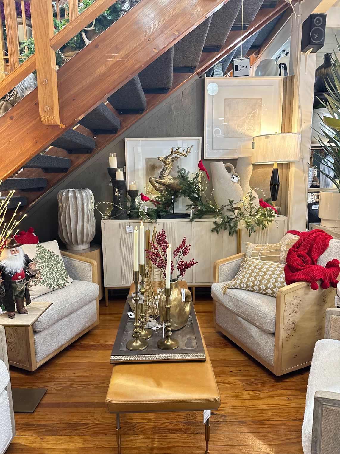 Decorated living room with beige chairs, wooden staircase, floral arrangements, and a glass coffee table
