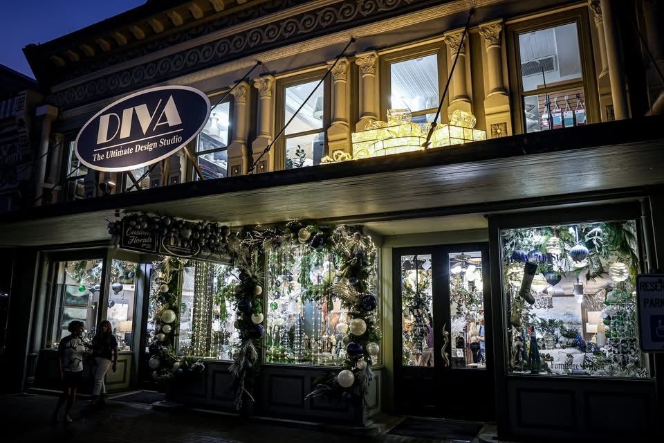 Nighttime storefront with glowing windows, hanging greenery, and an illuminated “DIVA” sign above the entrance