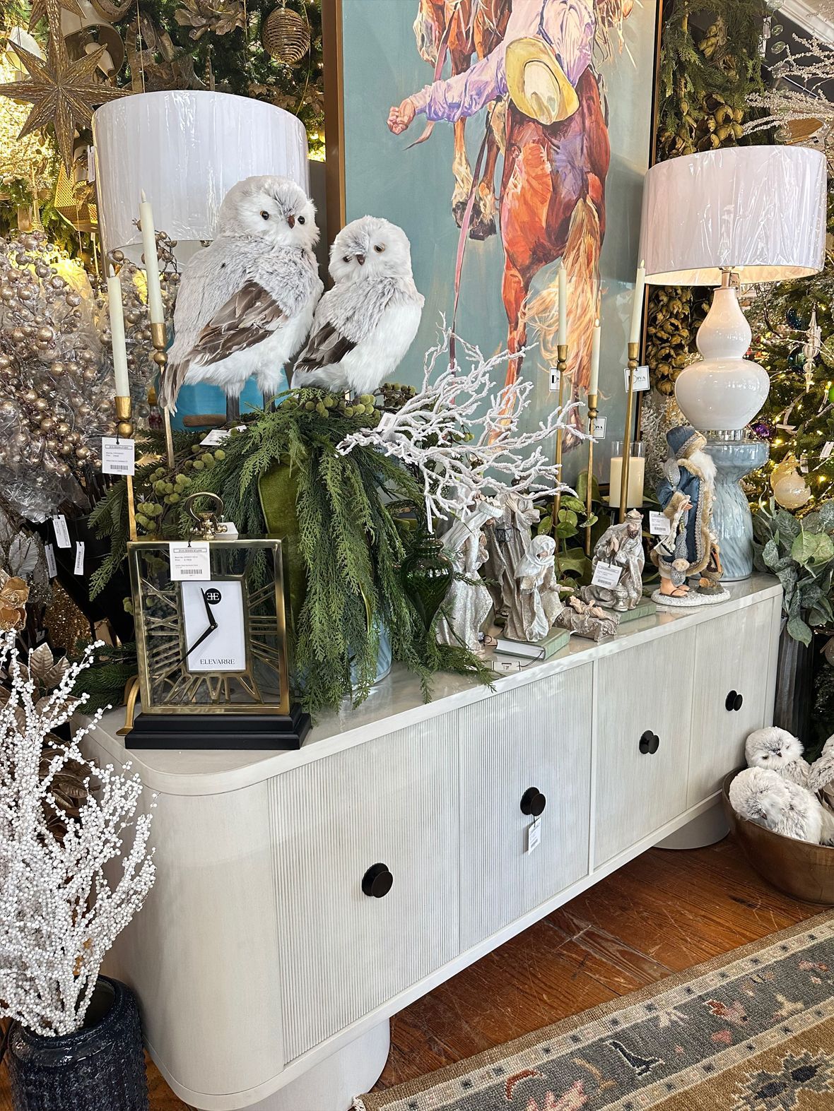 Decorated console with owl figurines, white lamps, greenery, and flowers in a cozy living room