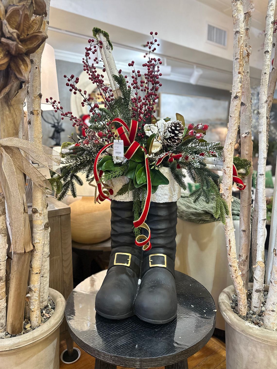 Black boots with buckles topped with festive red-and-green floral arrangement on a round table.