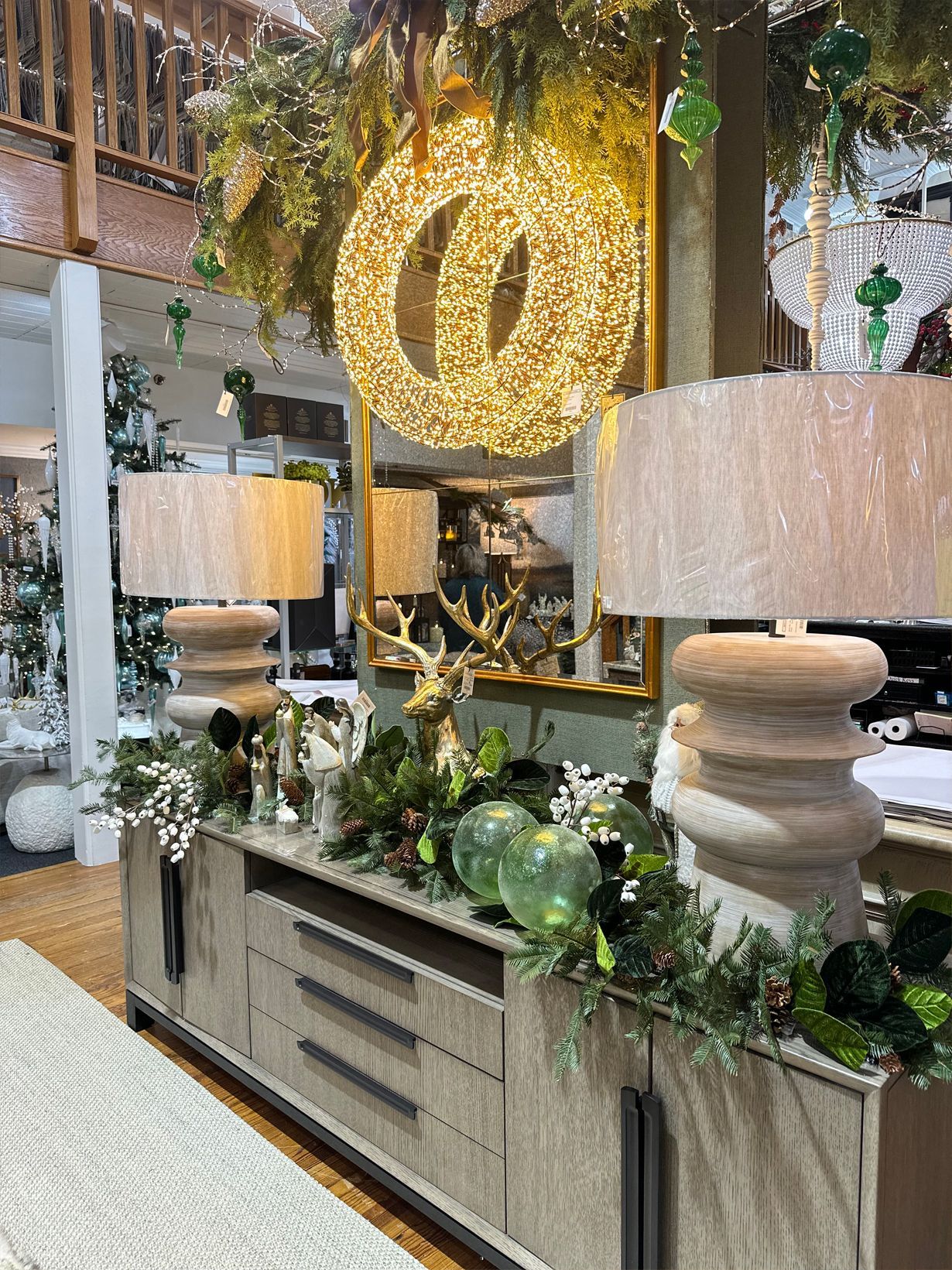 Elegant hotel lobby console with glowing ring chandelier, large lamps, and greenery on a wood sideboard