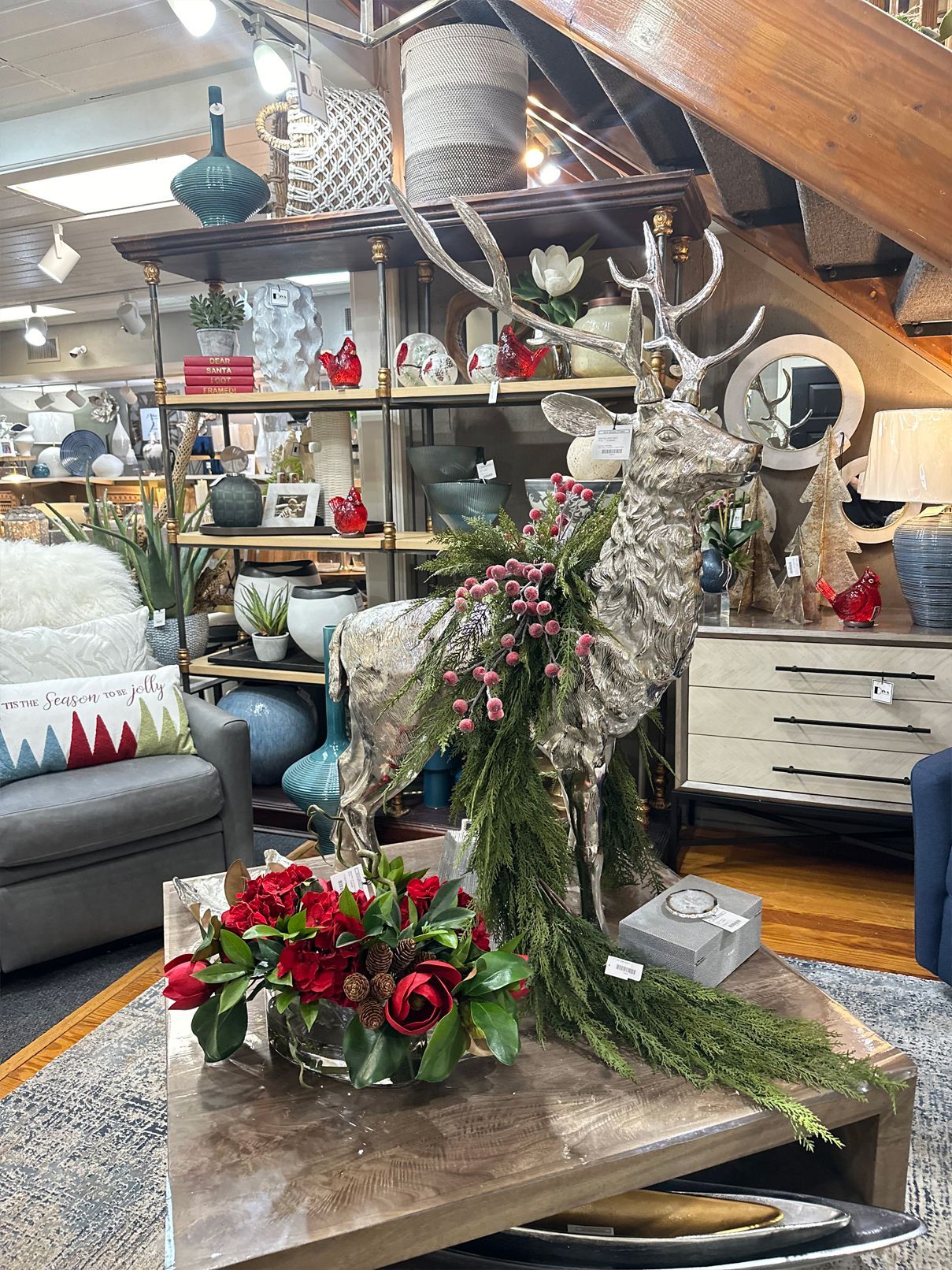 Cozy attic living room with holiday decor, a gray sofa, shelves, and a floral centerpiece on a coffee table