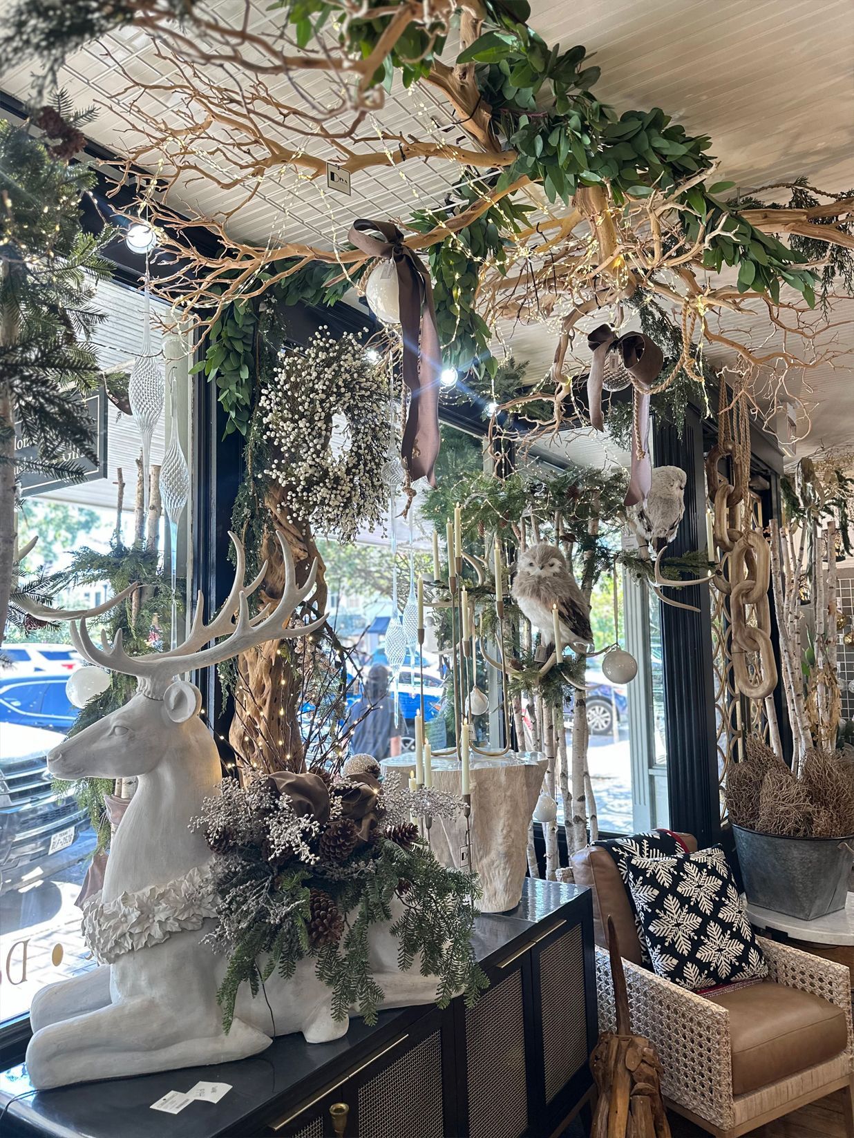 Decorative store display with hanging plants, driftwood, white animal sculptures, and a patterned chair